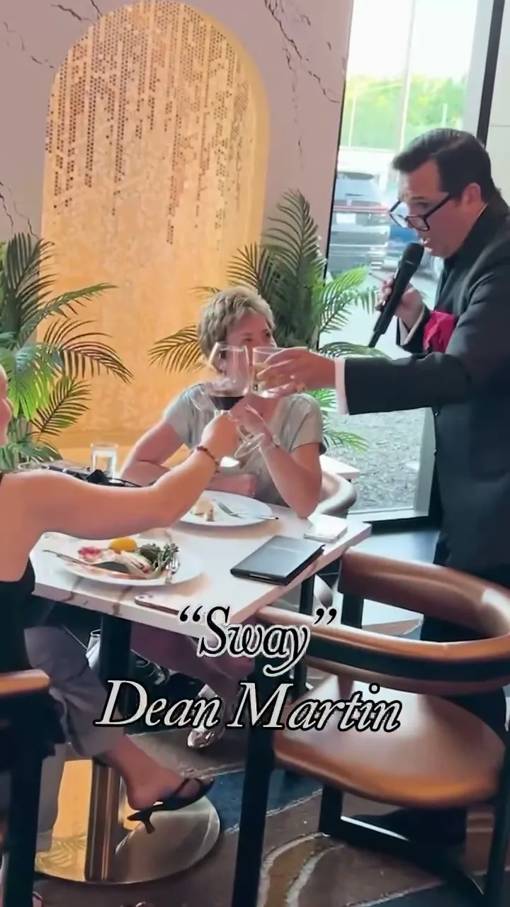 The singer toasting guests at their table by the window